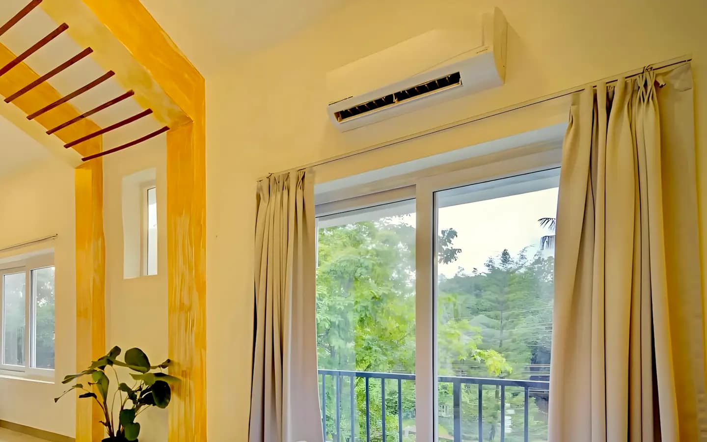 Aparelho de ar-condicionado split branco preso na parede de uma sala, perto de uma janela com cortinas
