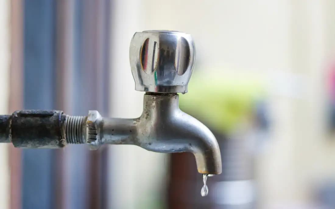 Torneira de metal com gota de água saindo da bica